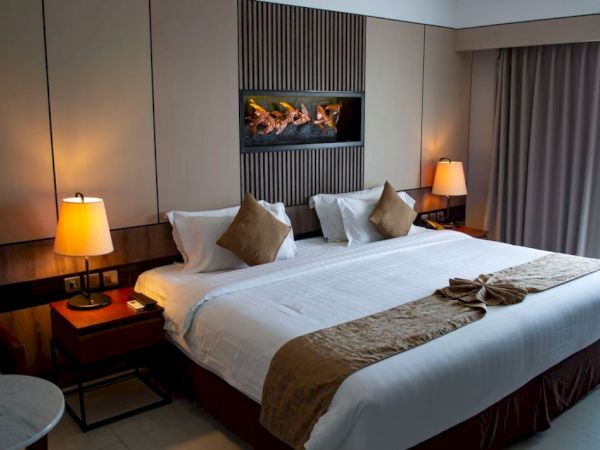 A cozy hotel room with a large bed, warm lighting, decorative pillows, wall art, and curtains.