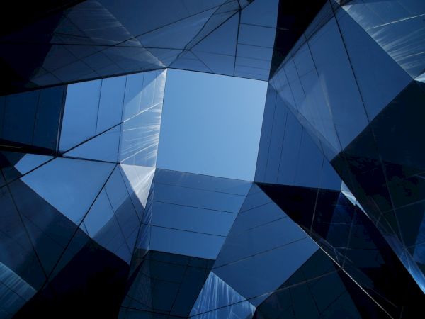 Abstract perspective of modern glass buildings reflecting a clear blue sky, forming geometric patterns.