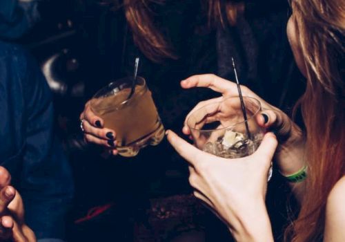 A group of people laughing and holding cocktails, with one person's hand covering their mouth, suggesting a cheerful social gathering.