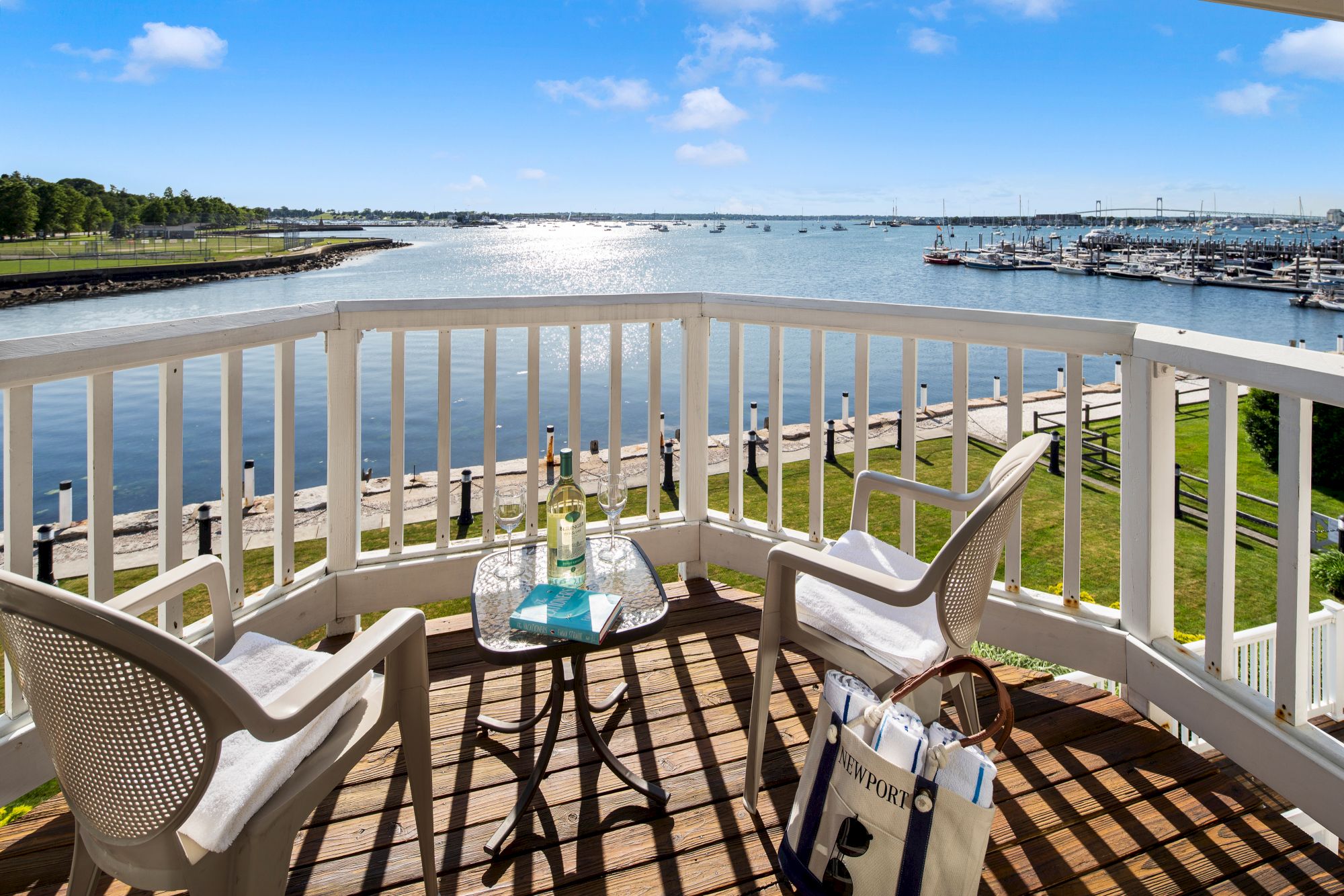 A scenic ocean view from a balcony with two chairs, a small table with drinks and a book, and a bag on the floor.