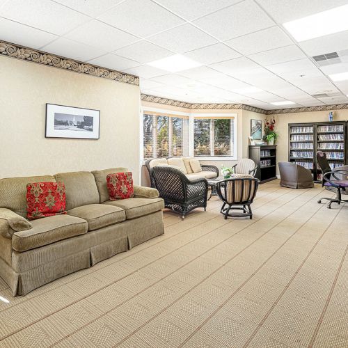 A spacious living room with a sofa, armchairs, large windows, a bookshelf, a desk, and a patterned carpet, creating a cozy atmosphere.