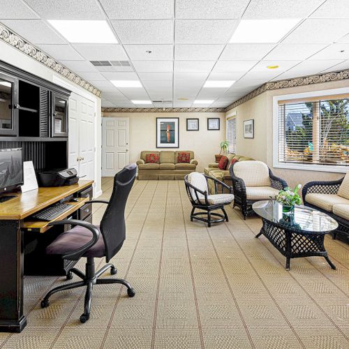 This image shows a well-lit office lounge with a desk, chairs, couches, and large windows letting in natural light.