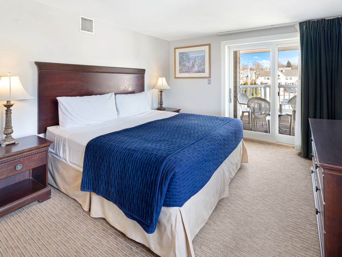 A cozy hotel room with a king-sized bed, two bedside tables with lamps, a dresser, and a balcony view.