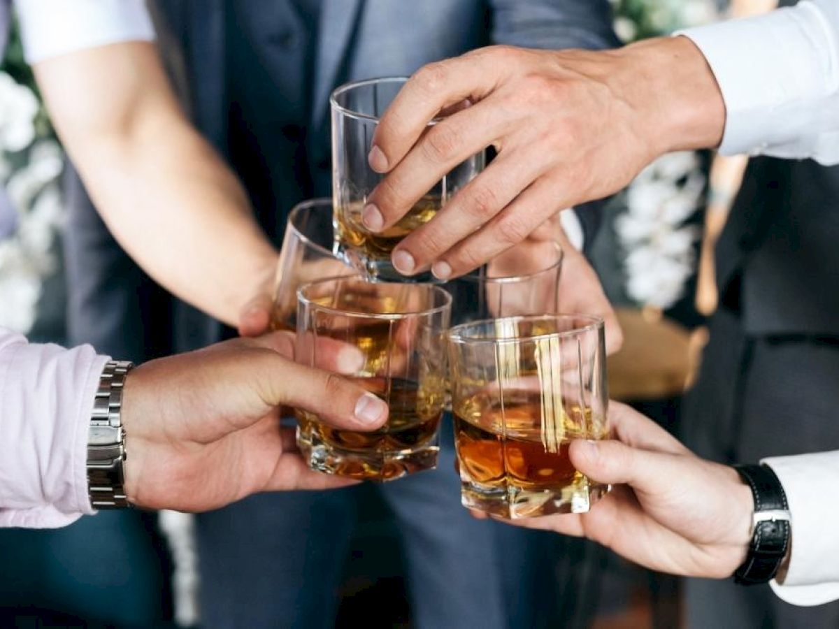 A group of people clink glasses filled with whiskey in a celebratory gesture, suggesting a toast or celebration.