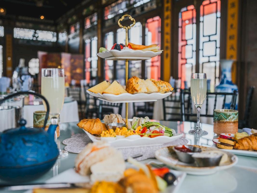 A lavish tea-time spread: a three-tiered platter of pastries, scones, and finger sandwiches with champagne flutes and a teapot in an elegant dining room.