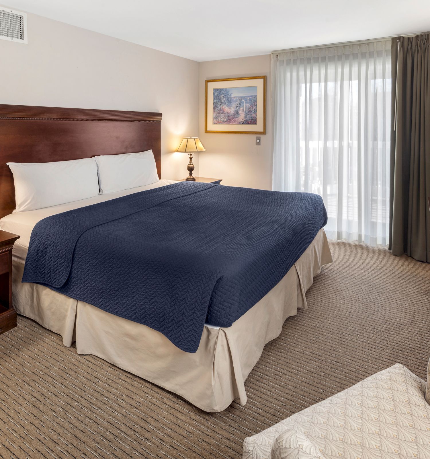 The image shows a hotel room with a large bed, two lamps on nightstands, a dresser, a chair, and a window with curtains.
