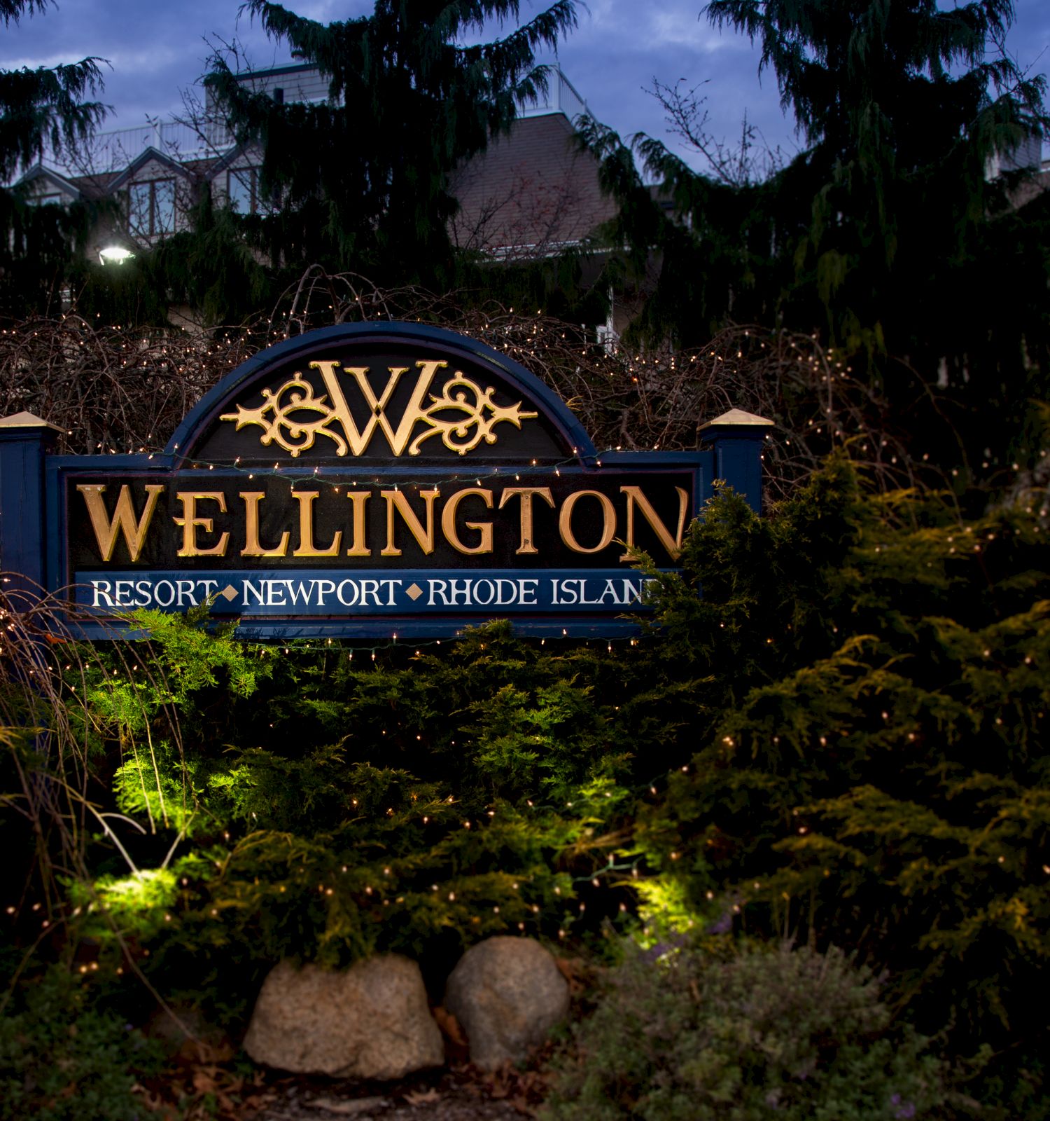 A sign for the Wellington Resort in Newport, Rhode Island, surrounded by trees and bushes with evening lighting.