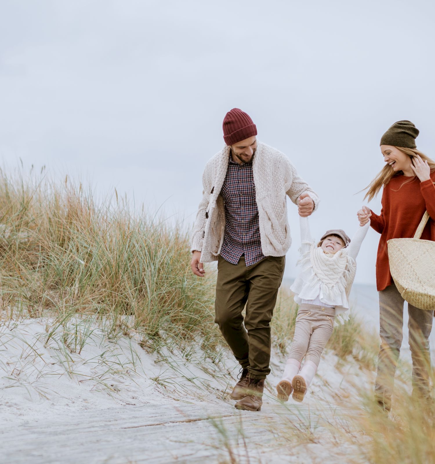 A family stroll on a sandy beach, a man, woman, and child holding hands and walking together along dunes.