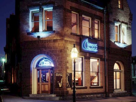 A lit brick pub at night with blue neon signs, arched windows, and a streetlamp in front, inviting warm glow and cozy atmosphere.