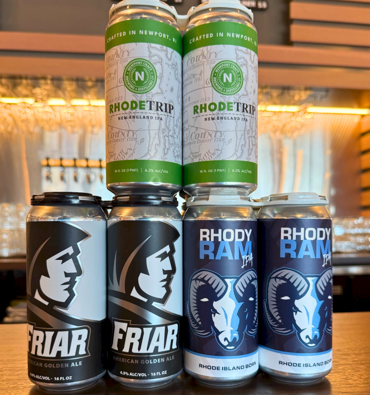 Two rows of beer cans on a bar counter: Rhode Trip pale ale tops, plus dark FRIAR and blue Rhode Ram cans ready to enjoy.
