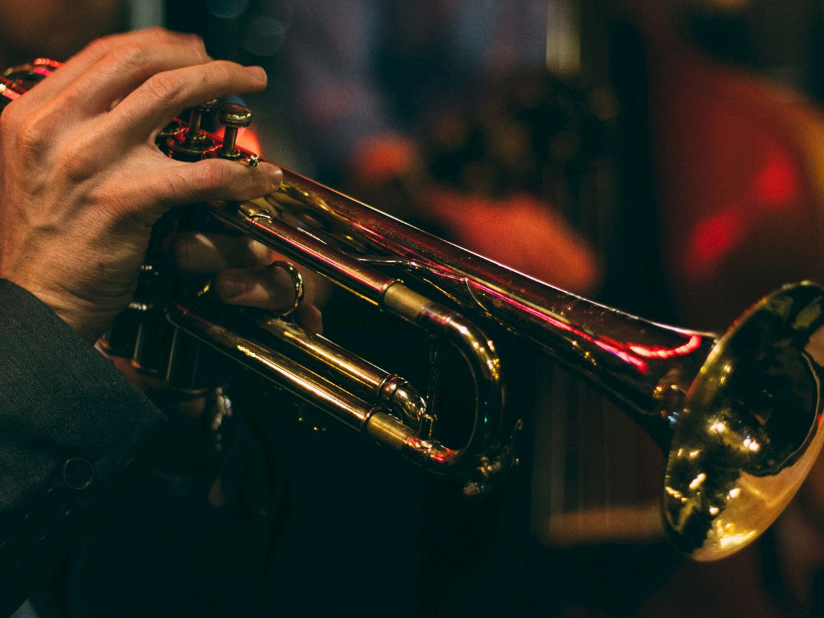 A musician&rsquo;s hands playing a brass trumpet onstage under colorful lights.