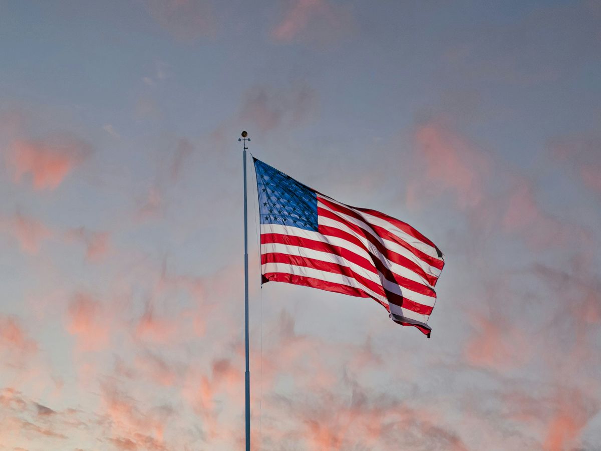 An American flag waving on a flagpole against a pastel sunset sky, rippling softly in the breeze, patriotic and peaceful.