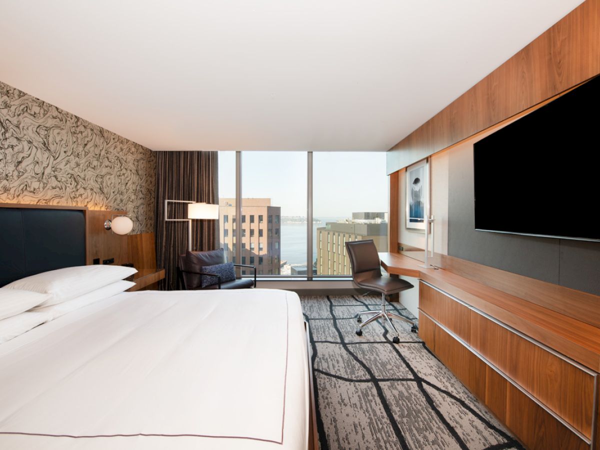 A modern hotel room with a large bed, a desk and chair, a flat-screen TV, and a city view through the window completes the scene.